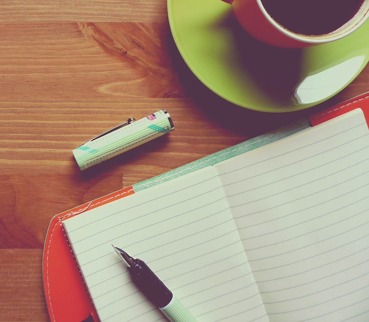 Caderno aberto, caneta e uma xícara sobre uma mesa de madeira